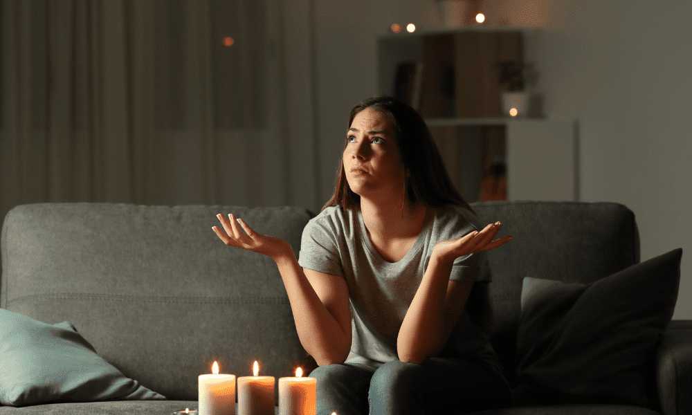 A frustrated woman is sitting in the dark with lit candles during blackout.