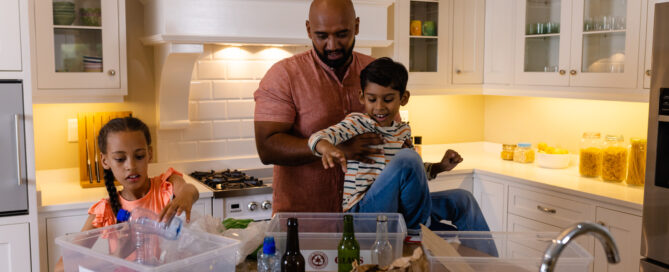 District Energy family recycling at home with kids sorting plastic, glass, and paper, highlighting sustainable home choices for eco-friendly living.